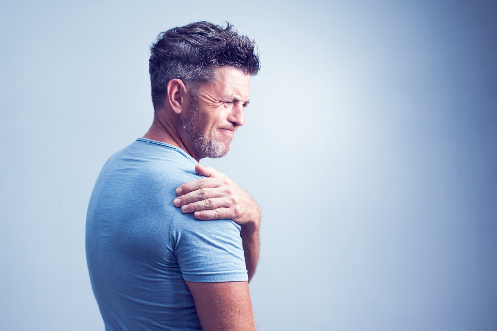 Middle-aged man holding her shoulder while grimacing in pain.