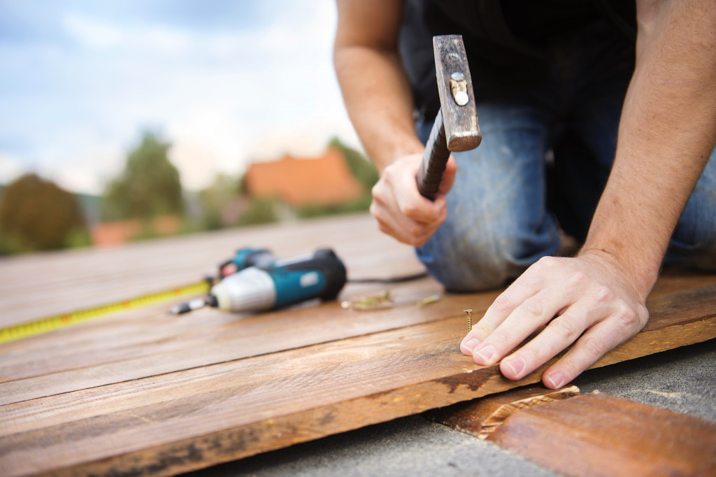 Handyman installing wooden flooring in patio, working with hammer