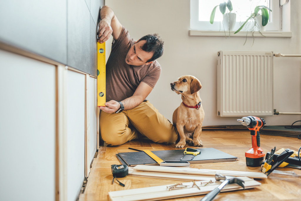 a man scaling the wall for measurements with tools and a puppy on his side
