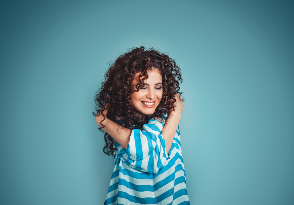 Young woman wearing a striped shirt smiling while hugging herself.