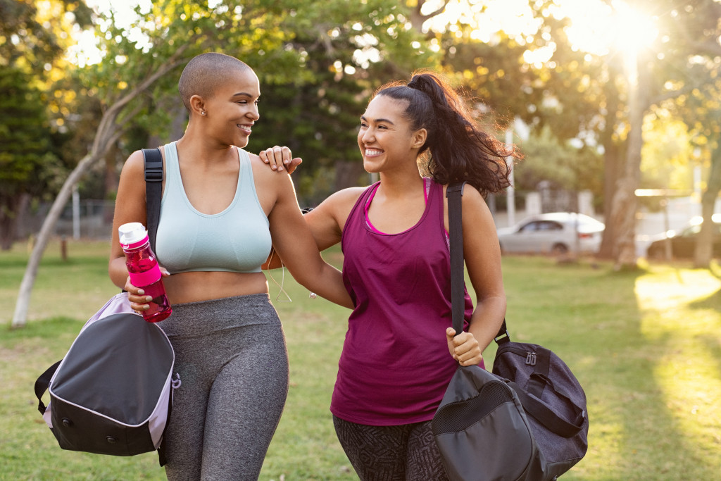 women smiling while carrying gym bags outdoors in the morning