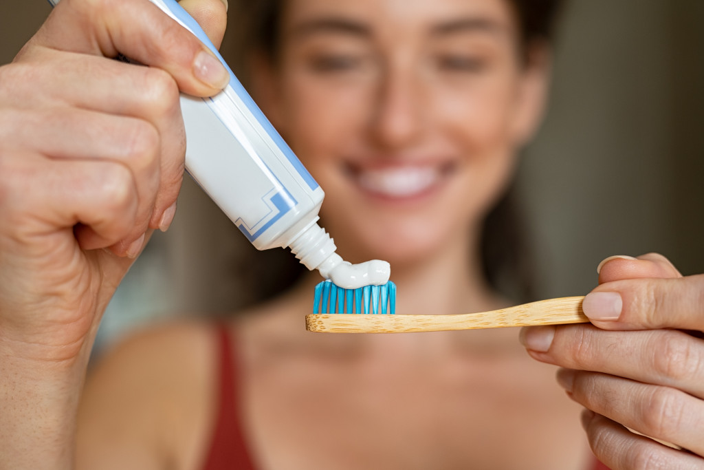 Closeup of girl hands squeezing toothpaste on ecological wooden brush.