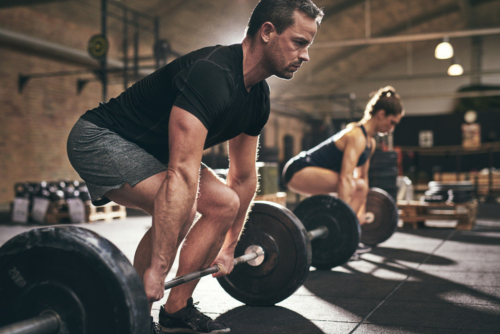 man and woman in gym doing deadlifts with barbells