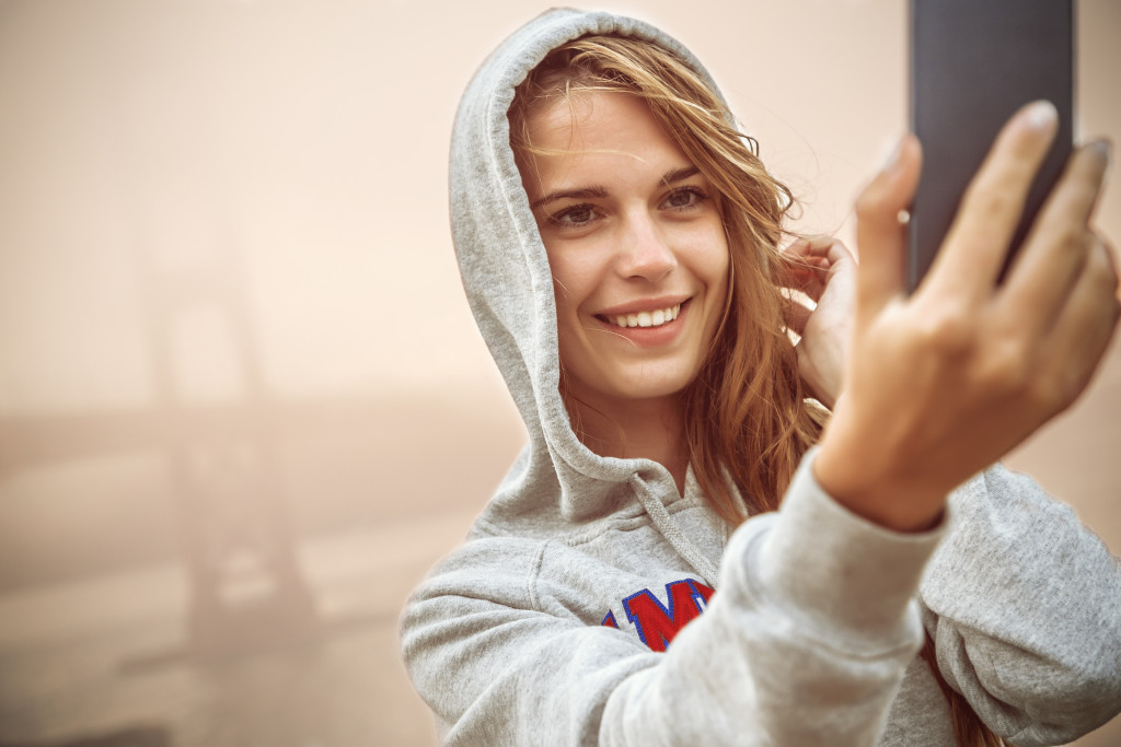 Young woman taking a selfie in front of a fog-covered bridge.