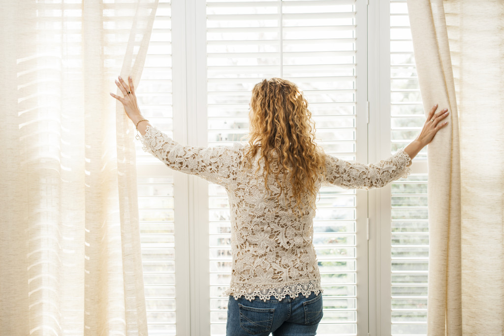 a woman opening a curtain to let in light