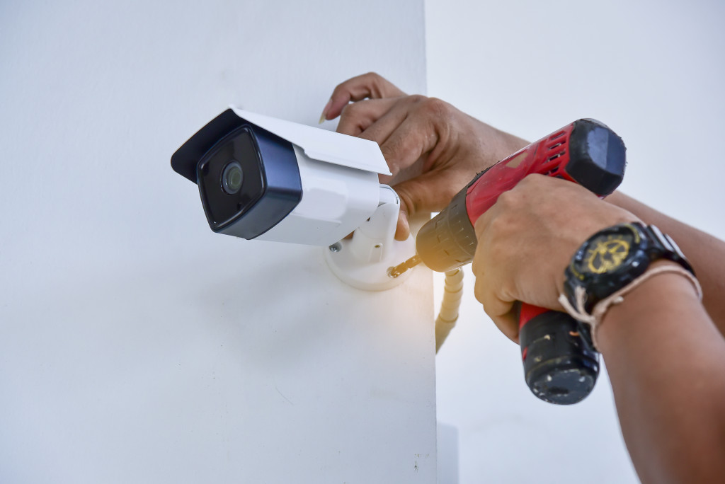 A person installing a surveillance cam on a white wall