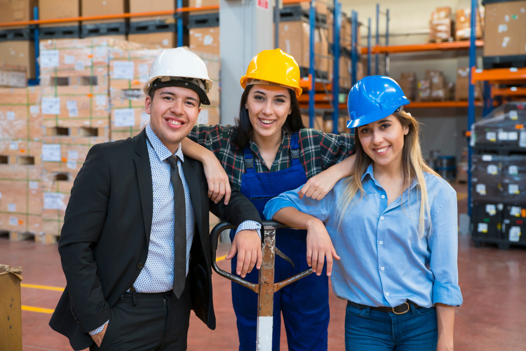 Two female and one male employee smiling while inside a warehouse.