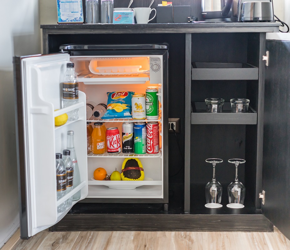 A mini bar with a small fridge, drinks, and glasses