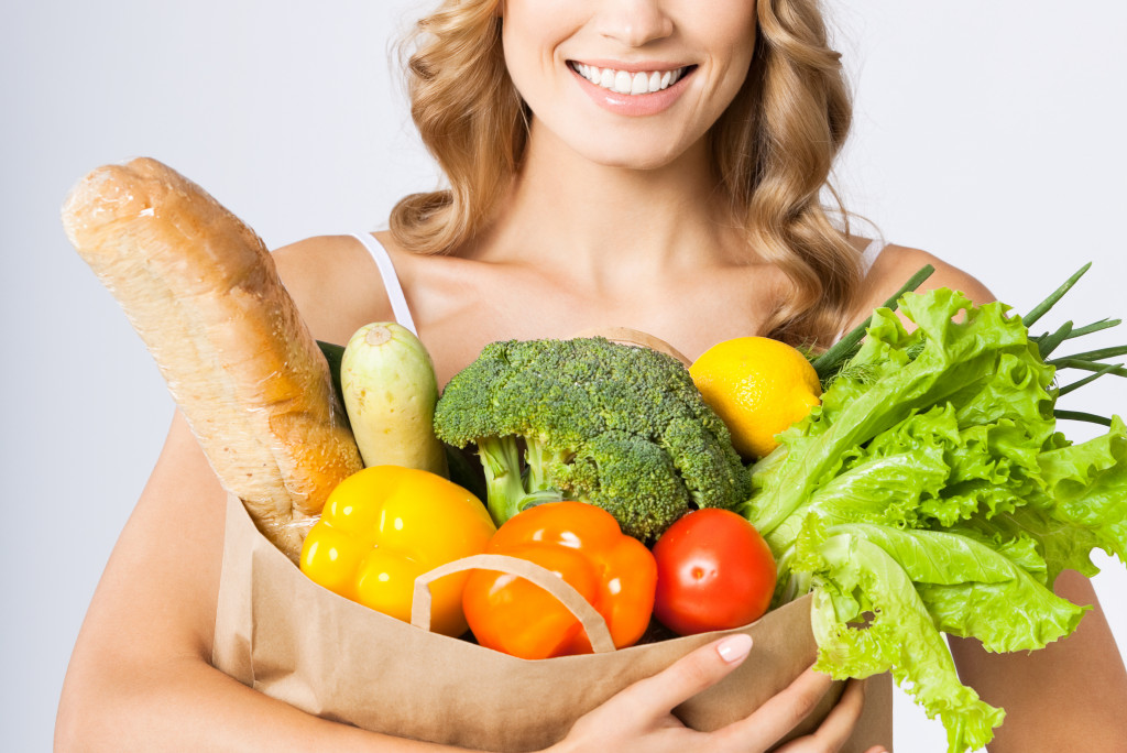 A woman hugging a grocery bag with fruits, vegetables, and bread