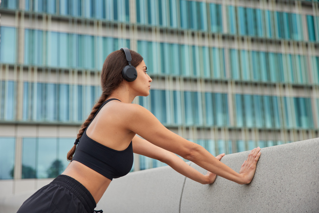 Young woman leaning on a concrete wall while wearing headphones.