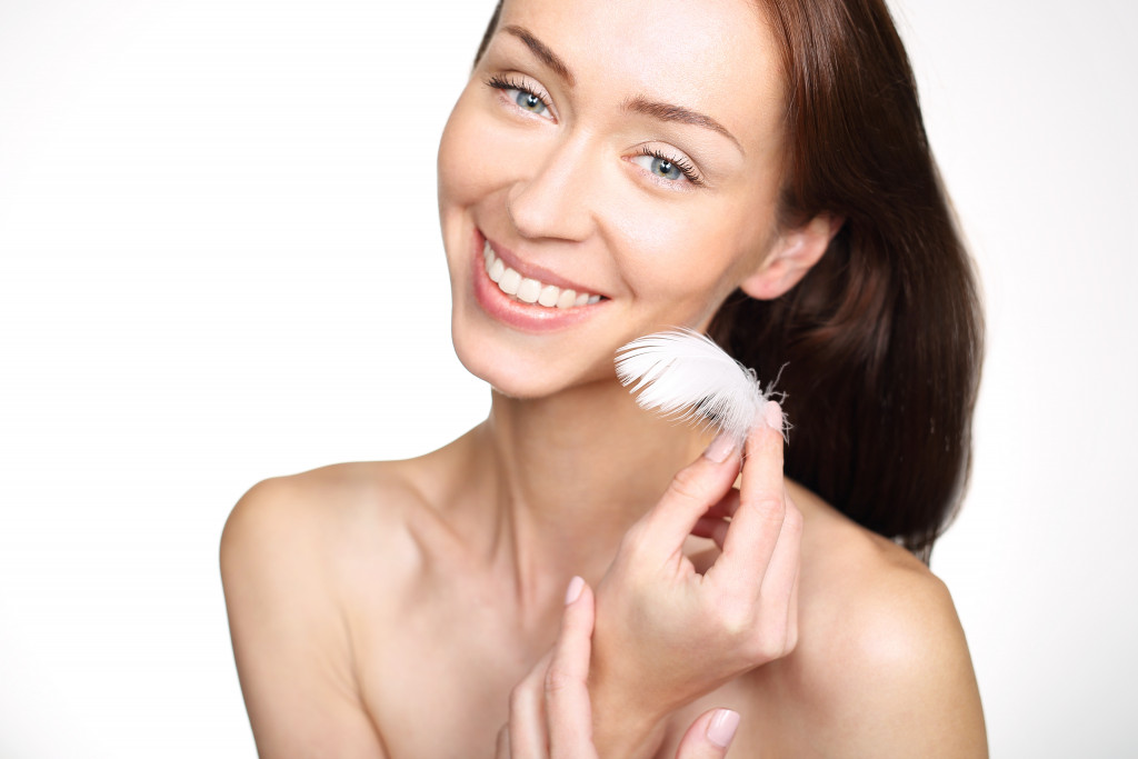 Young woman smiling while touching her face with a feather.