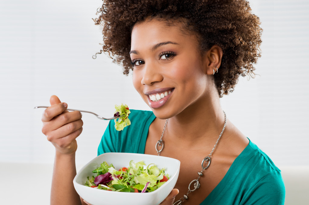 Young woman eating a bowl of salad at home.